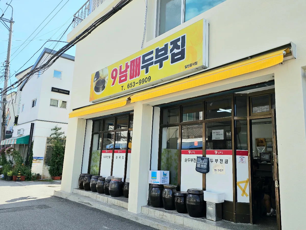 クナムメ・トゥブジプ — 黄色い看板と店先に並ぶ甕