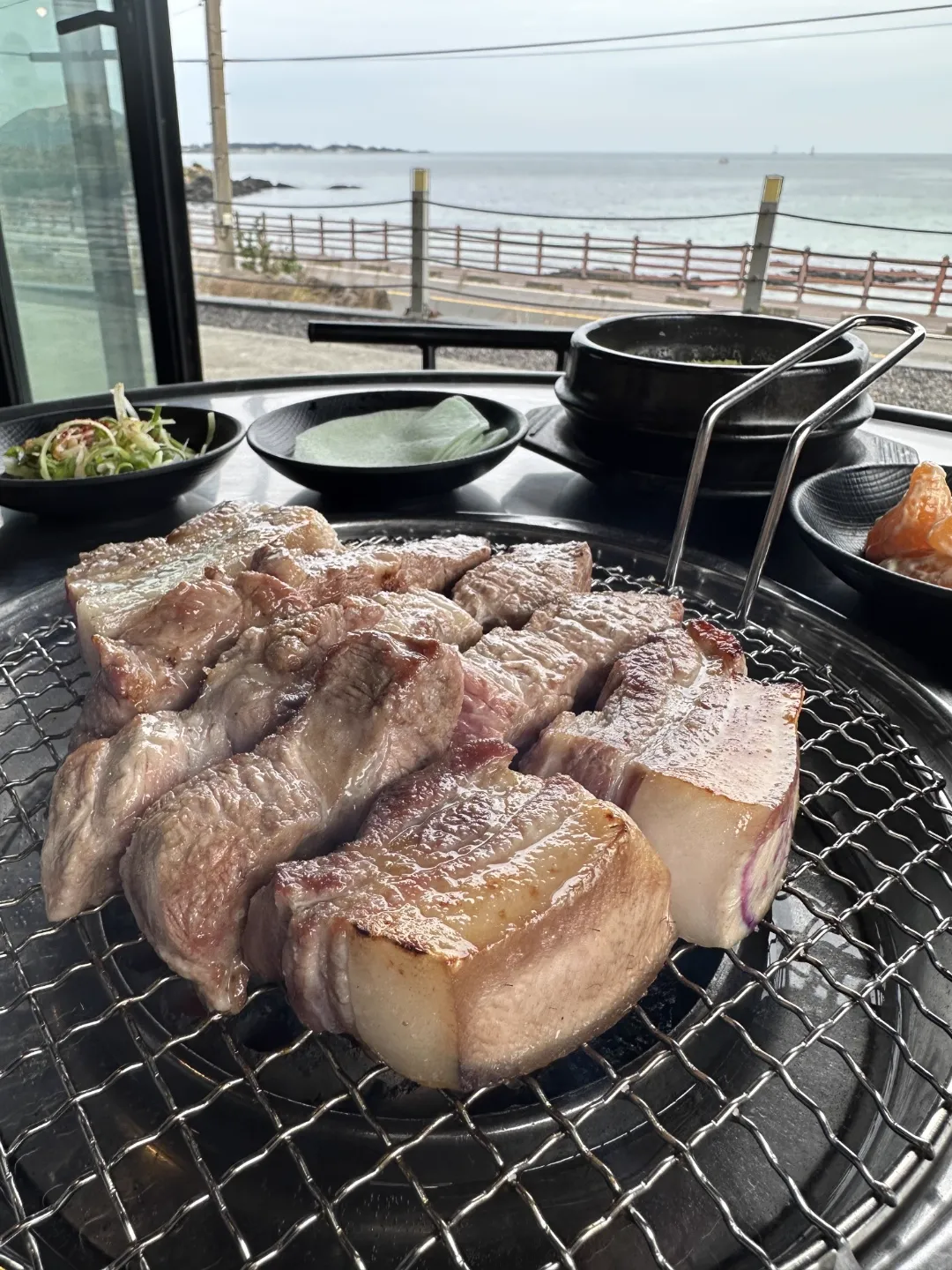 海を背景に網で焼く厚切り肉と土鍋