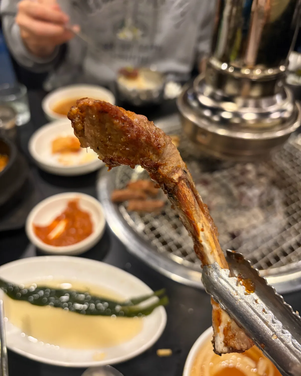 トングで持ち上げた骨付きサムギョプサル