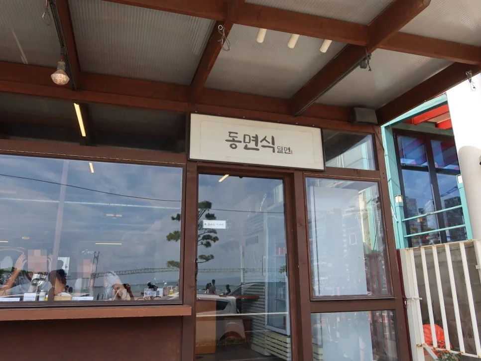 トンミョンシク・ミルミョン — 店名看板と窓越しに海が見える店先