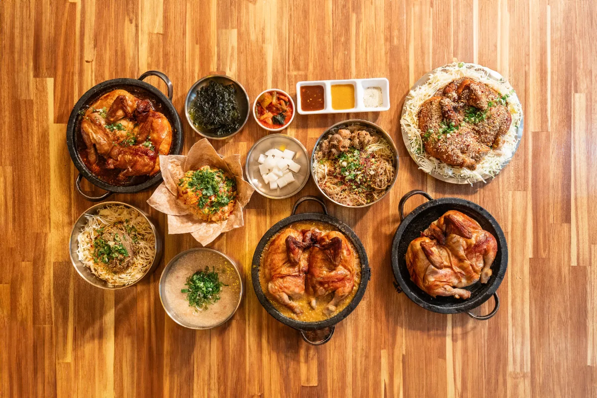 ヘバンチョンタッ 龍山解放村本店 — 丸鶏や麺、鶏粥など看板メニューを並べた食卓