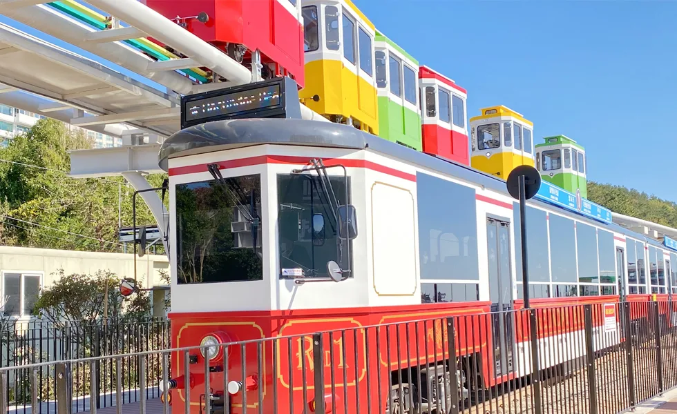 上の高架を走るカプセルと、下の線路に停まる赤い海辺列車