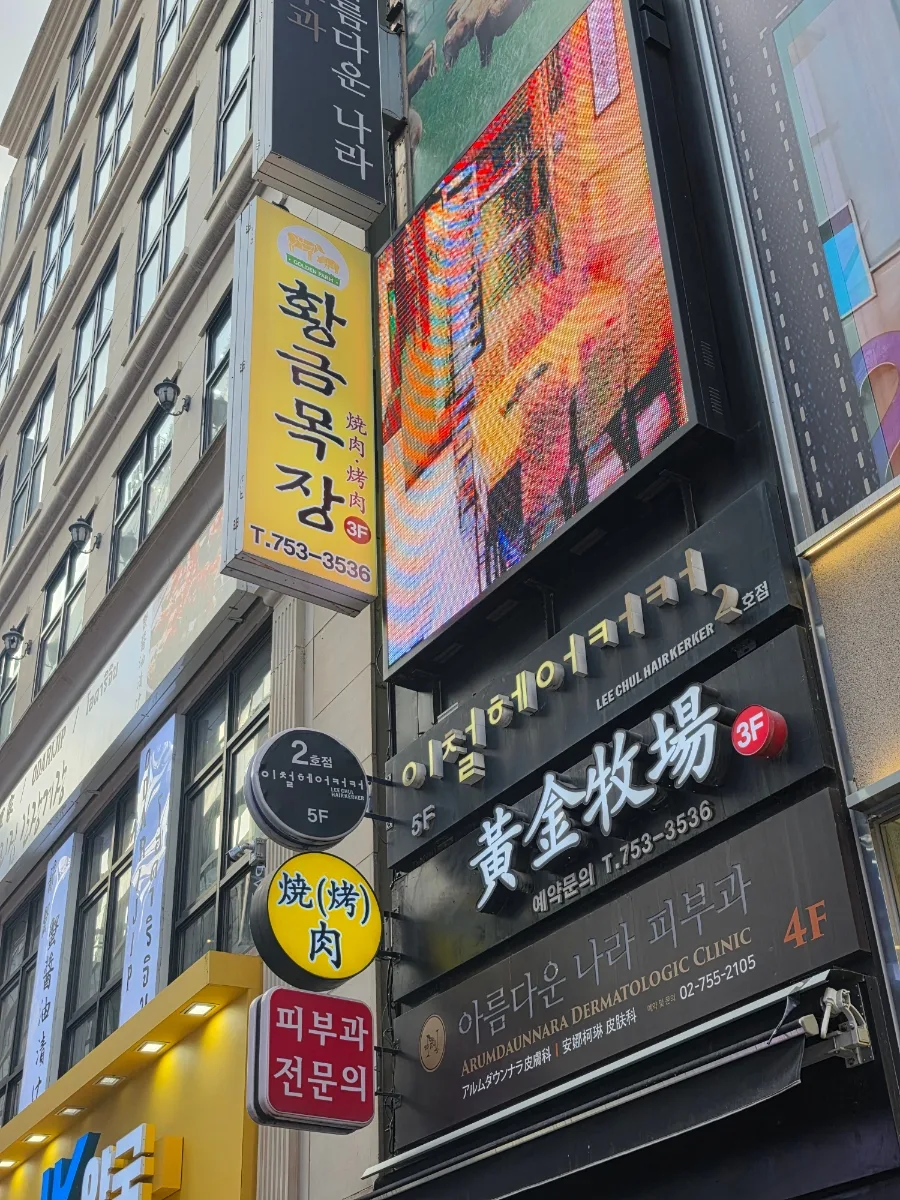 黄金牧場 明洞店 — ビルに掛かる黄色い縦看板