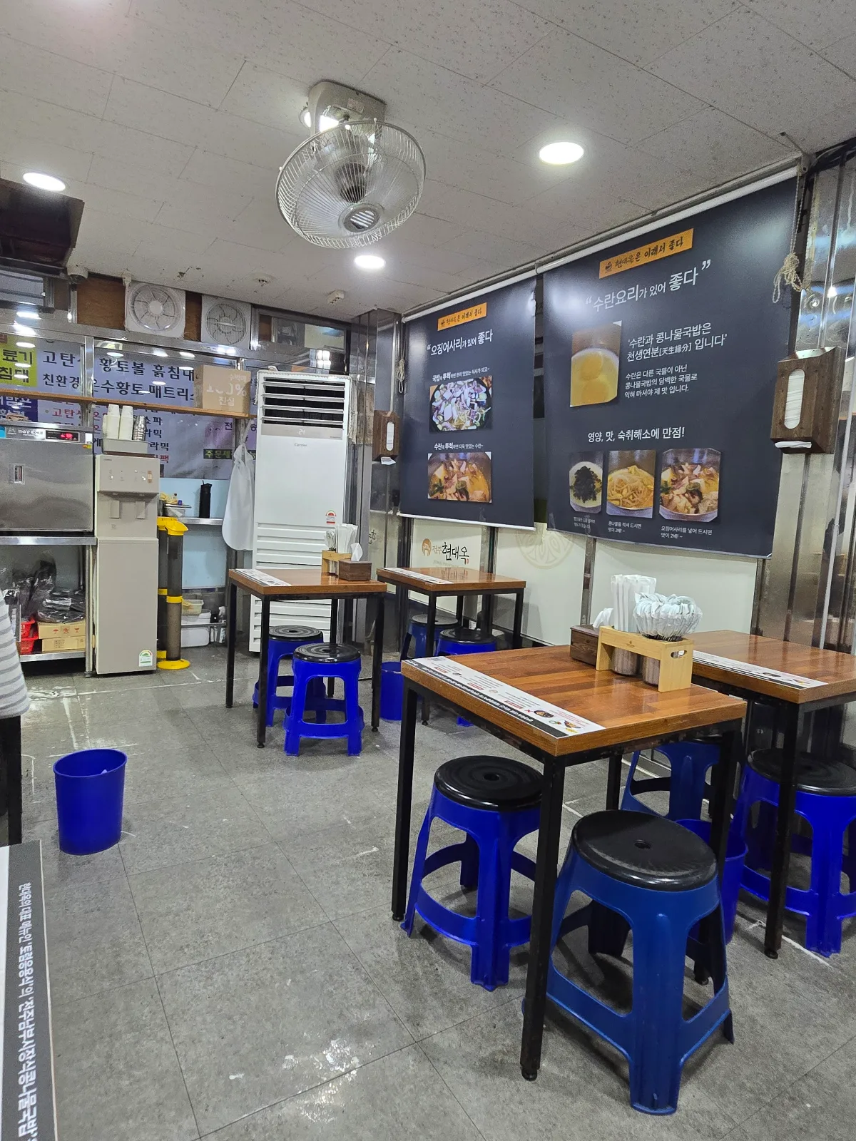 ヒョンデオク 南部市場店 — 木のテーブルと青い丸椅子