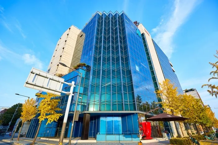 JYPエンターテインメント 本社 — 黄葉したイチョウと青いガラスの本社