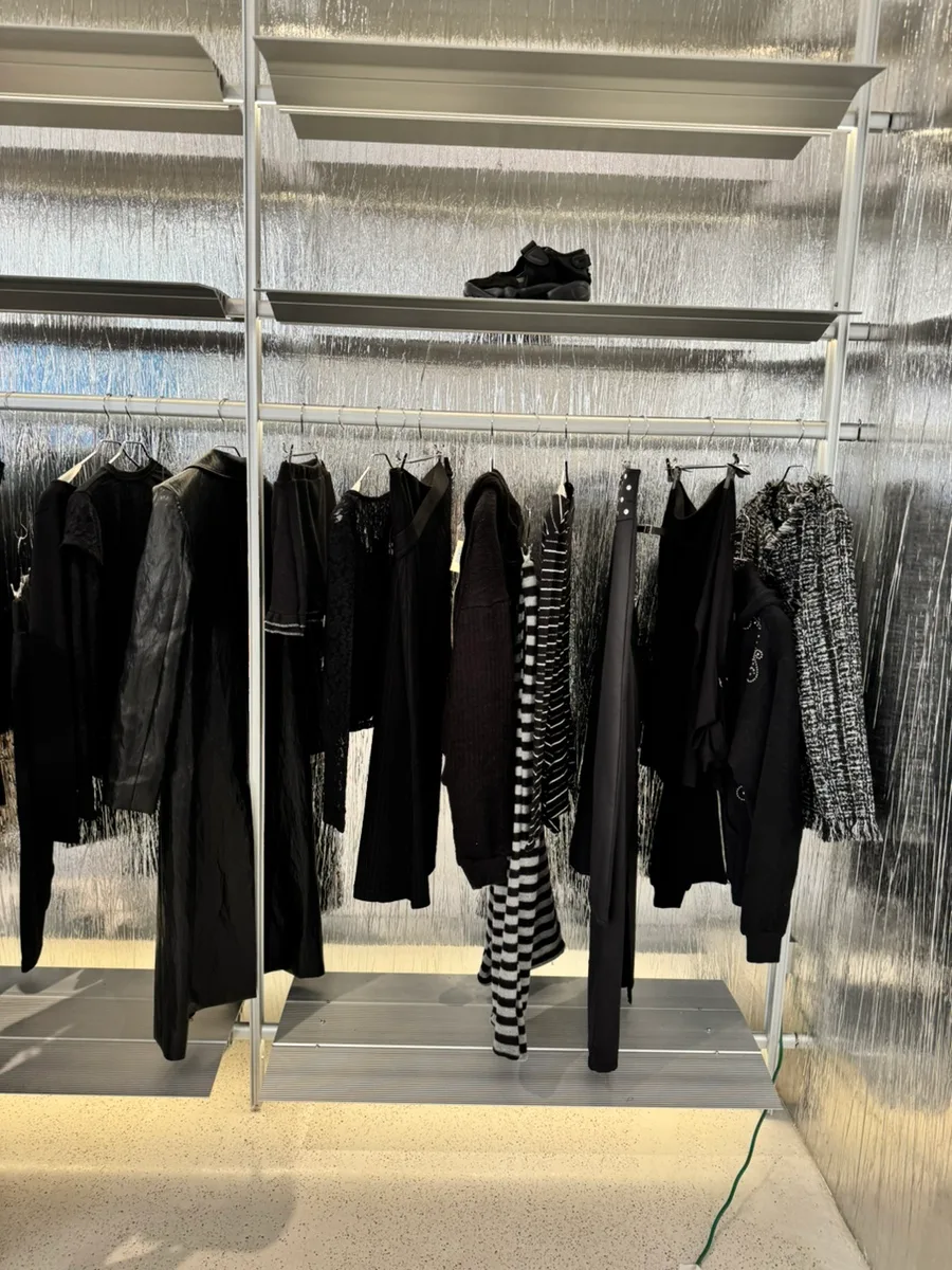 カシナ 聖水店 — 銀色の壁に並ぶ黒い服