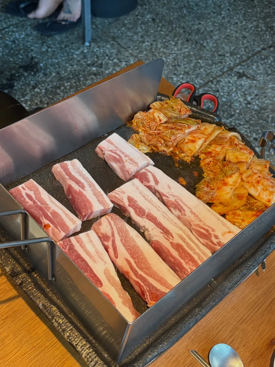 マッキムチ生サムギョプサル 延南店 — 油はね防止の板を立てた鉄板に並ぶ生の豚バラとキムチ