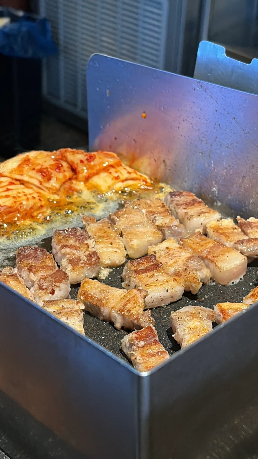 油はね防止の板の中で焼ける豚肉とキムチ