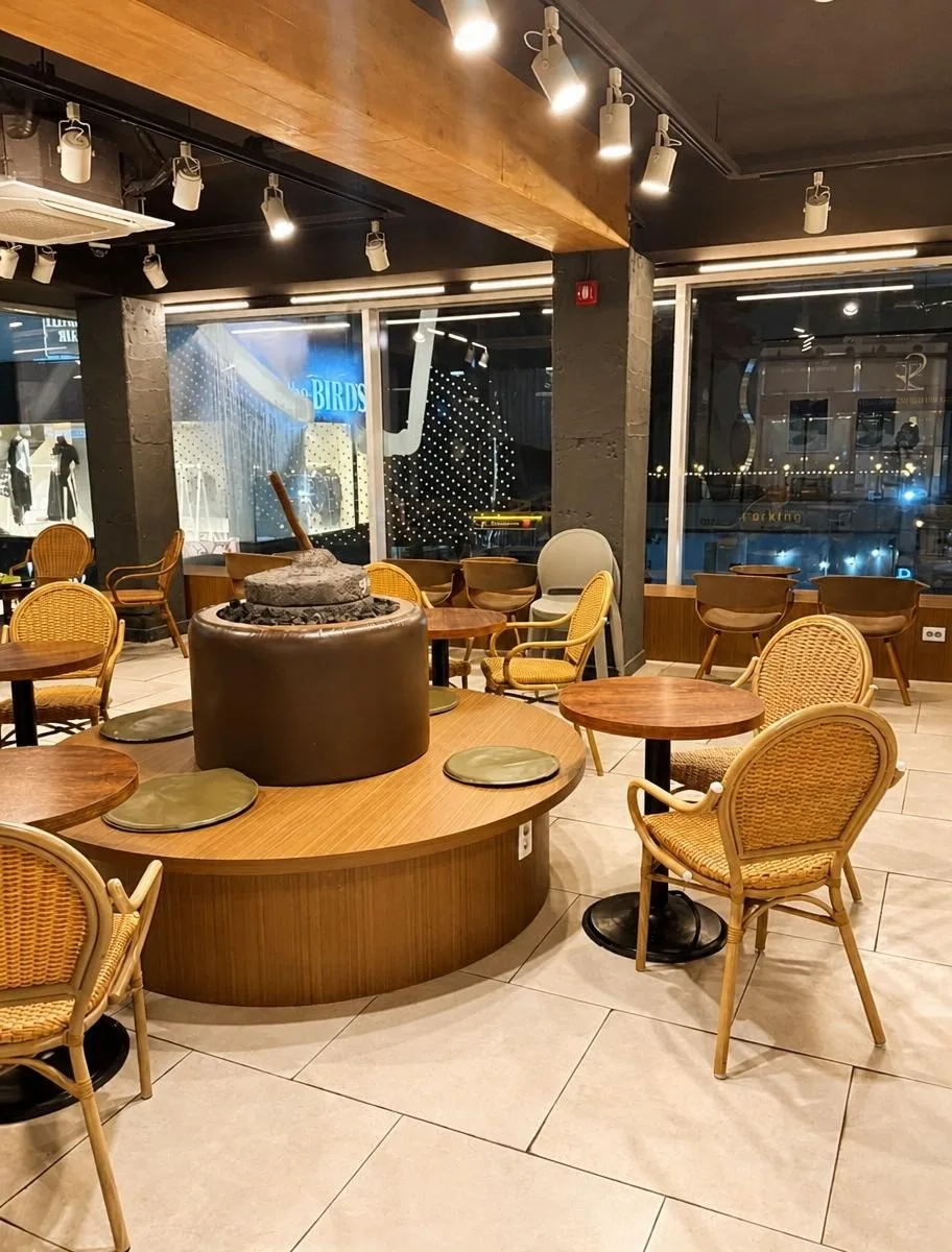 METCHA 明洞本店 — 石臼を囲む木のテーブルと籐椅子
