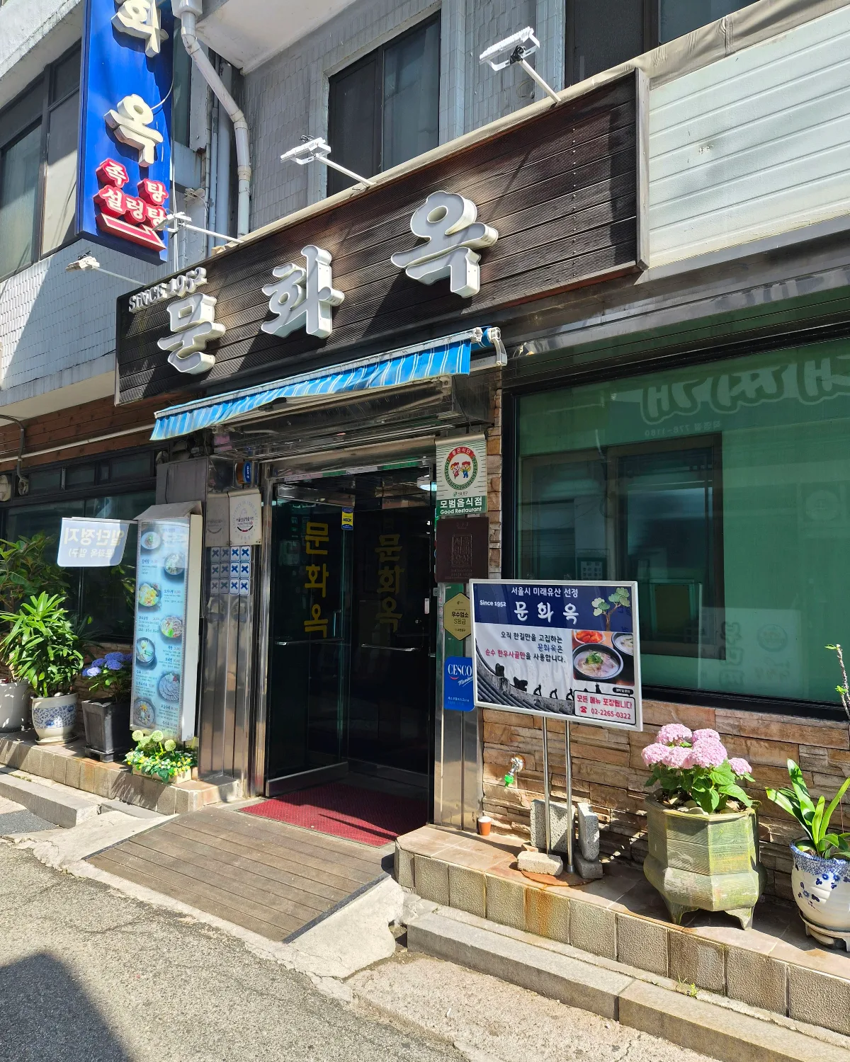 文化屋 — 文化屋の看板と鉢植えのある入口