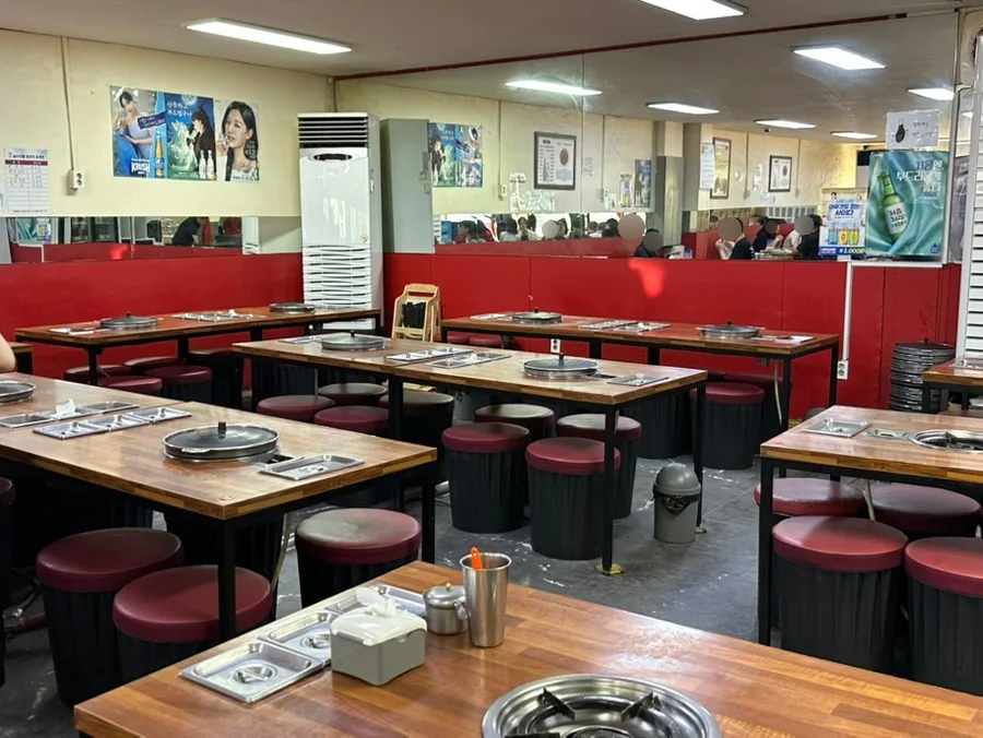 ナ・ジョンスンハルメチュクミ 龍頭店 — 鉄板付きの卓と赤い丸椅子