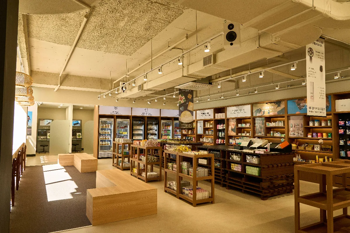 オプティマウェルネスミュージアム薬局 江南店 — 木製の棚とベンチが並ぶ売り場