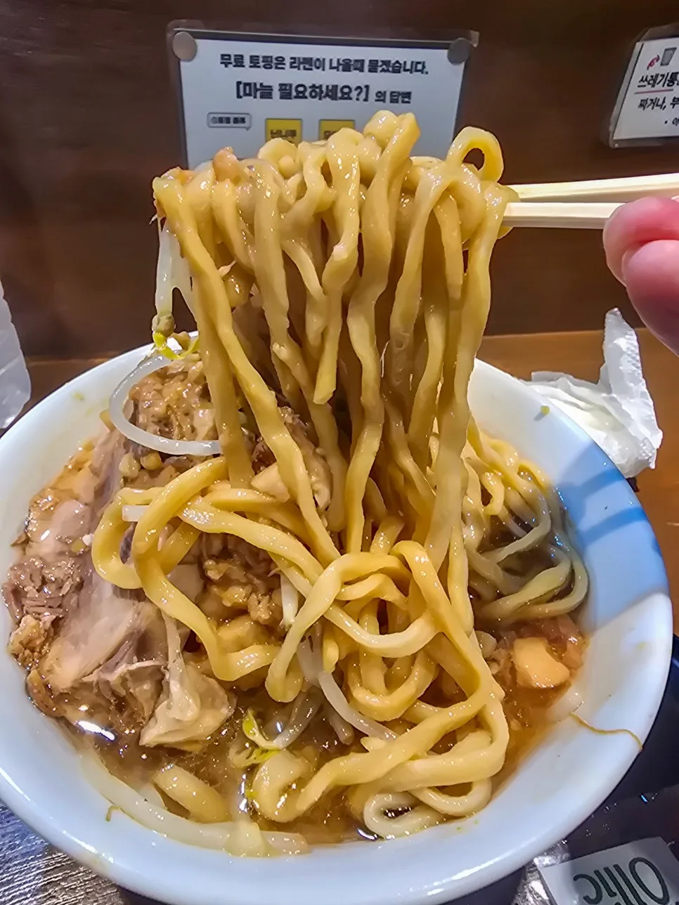 「ニンニク入れますか」の案内が貼られたカウンターと太麺