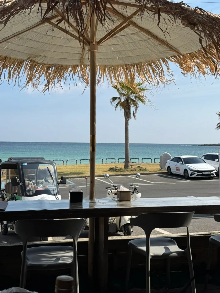 ソムソナイ 牛島本店 — わらぶきのパラソル越しに見えるハゴスドンの海