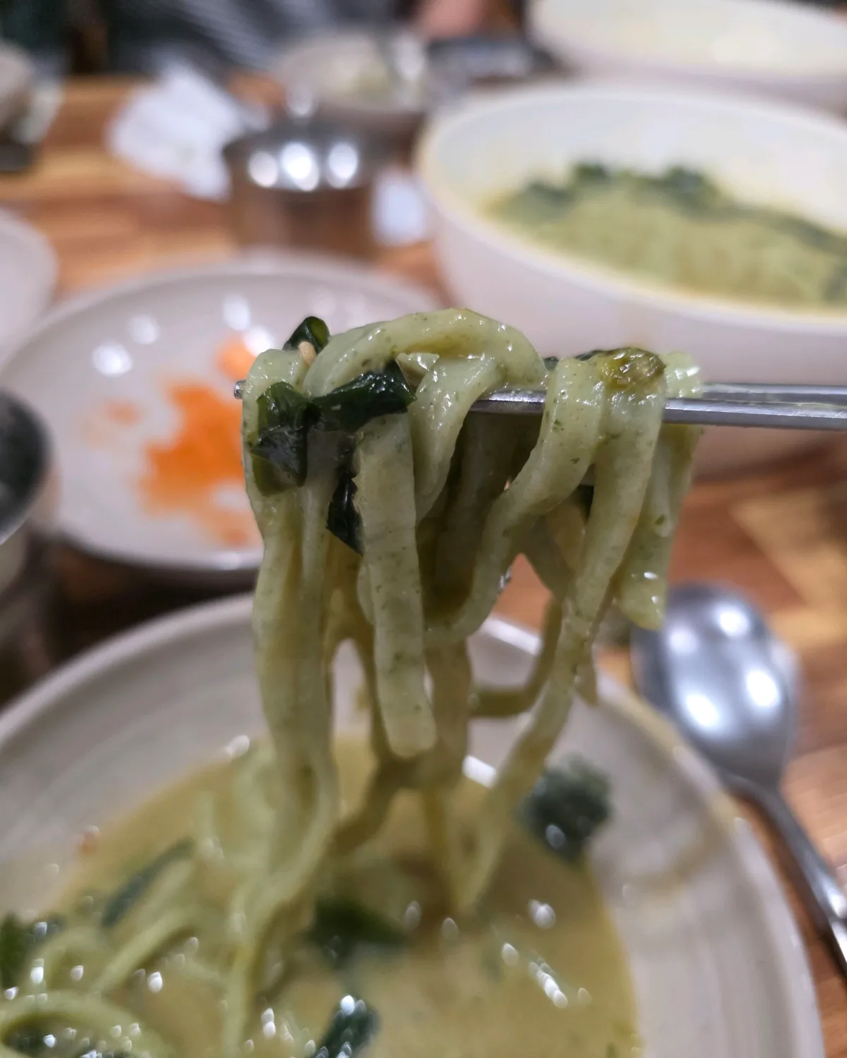 新済州ボマルカルグクス 本店 — 箸で持ち上げた緑色の自家製麺