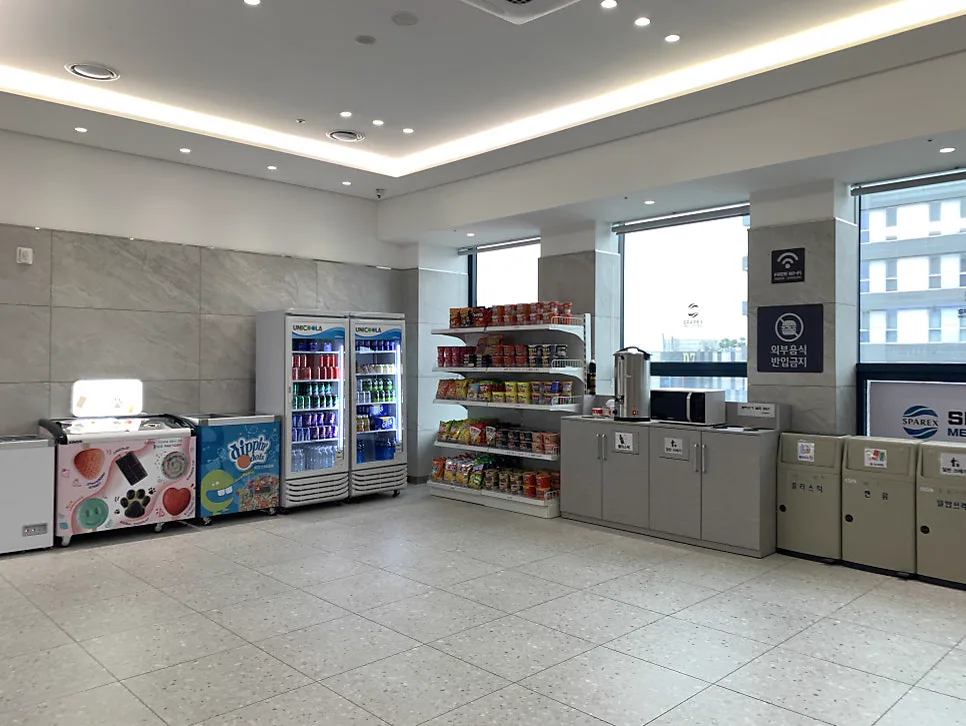 窓際に飲み物の冷蔵庫、カップ麺の棚、アイスケースが並ぶ売店コーナー