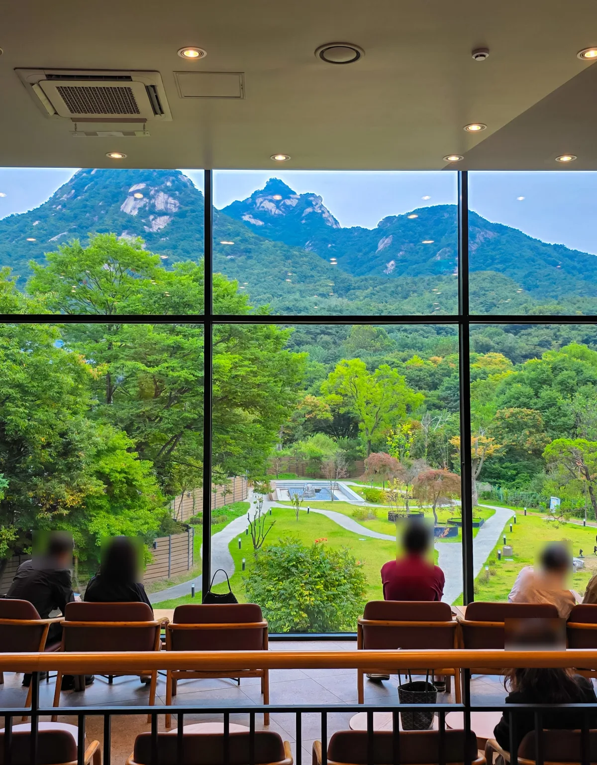 窓辺の席の向こうに北漢山の岩山と庭園が広がる、ザ北漢山店の店内