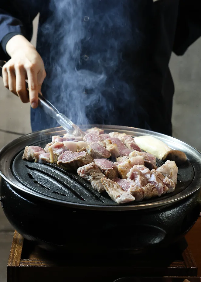 スタッフが炭火で豚肉を焼くところ