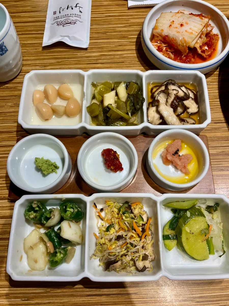 キムチ、ニンニクの漬物、シイタケ、もやしのナムルなどが小皿に並ぶ王妃家のおかず